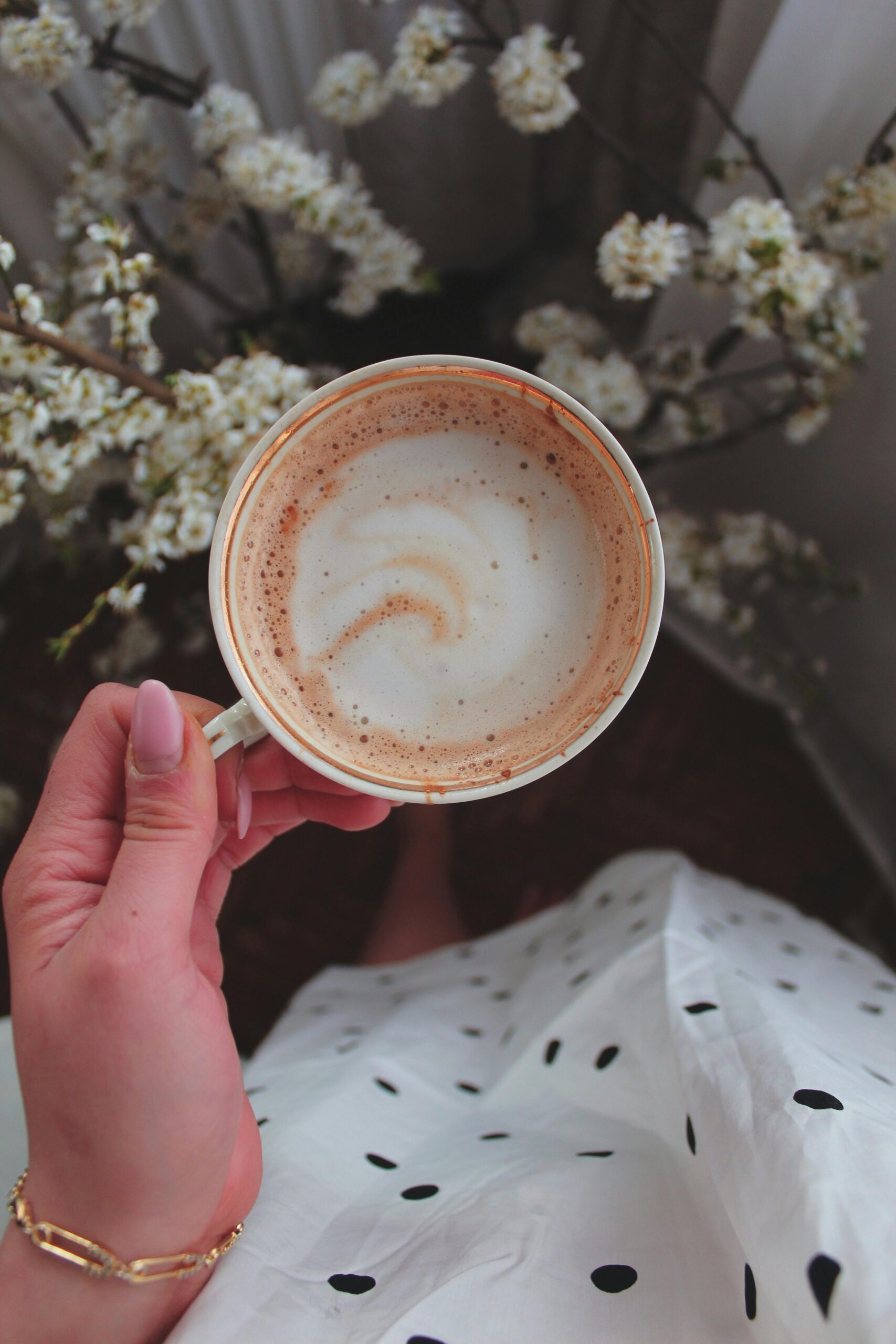 A hand holding a cappuccino cup above a floral background. Elegant and calming.