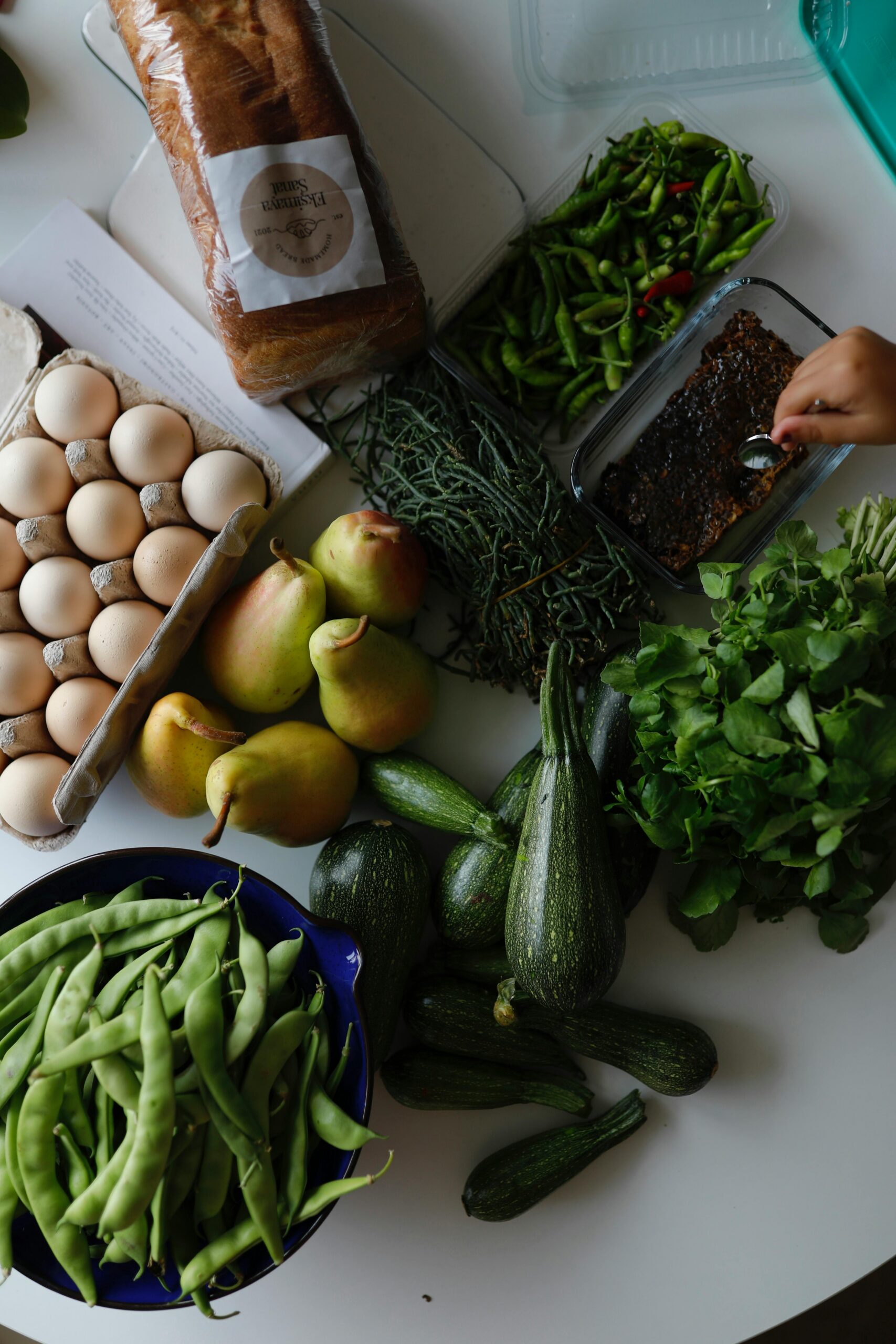 An appetizing flat lay of fresh eggs, pears, greens, and vegetables on a white surface.