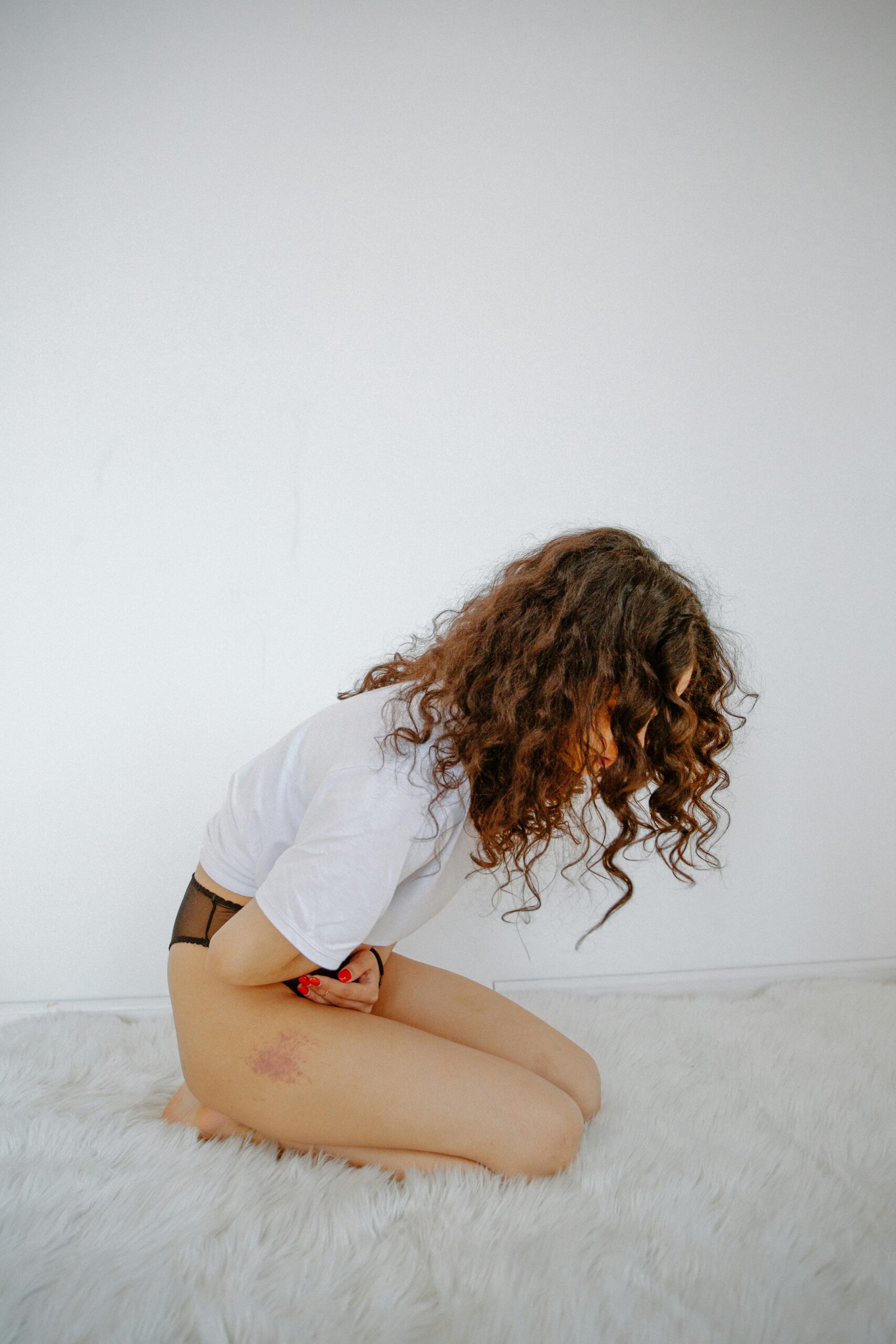 Woman holding stomach while kneeling, expressing discomfort from abdominal pain.