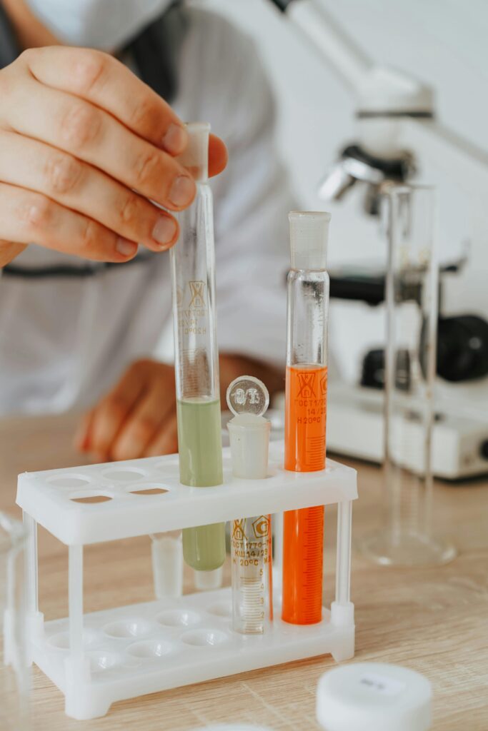 Close-up of scientist's hand arranging colorful test tubes with microscope in the background.